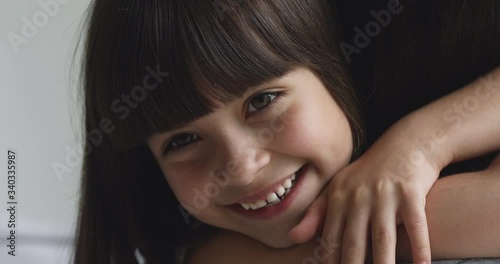 Close up head shot overjoyed adorable small preschool daughter embracing mommy, feeling happiness. Excited little cute adopted girl cuddling new mother nanny babysitter, showing love after reconcile.
