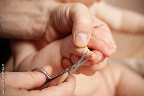  Dad cuts the nails on his daughter   s hands. Male hands with scissors cut off a child   s nail on a beige background.