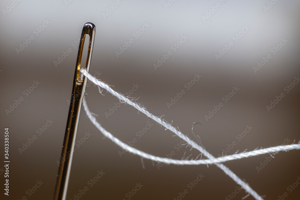 Fotografia macro de una aguja enebrada con hilo blanco