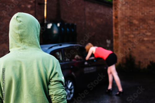 Man watches a prostitute talking to a potential customer in a car (posed by models) photo