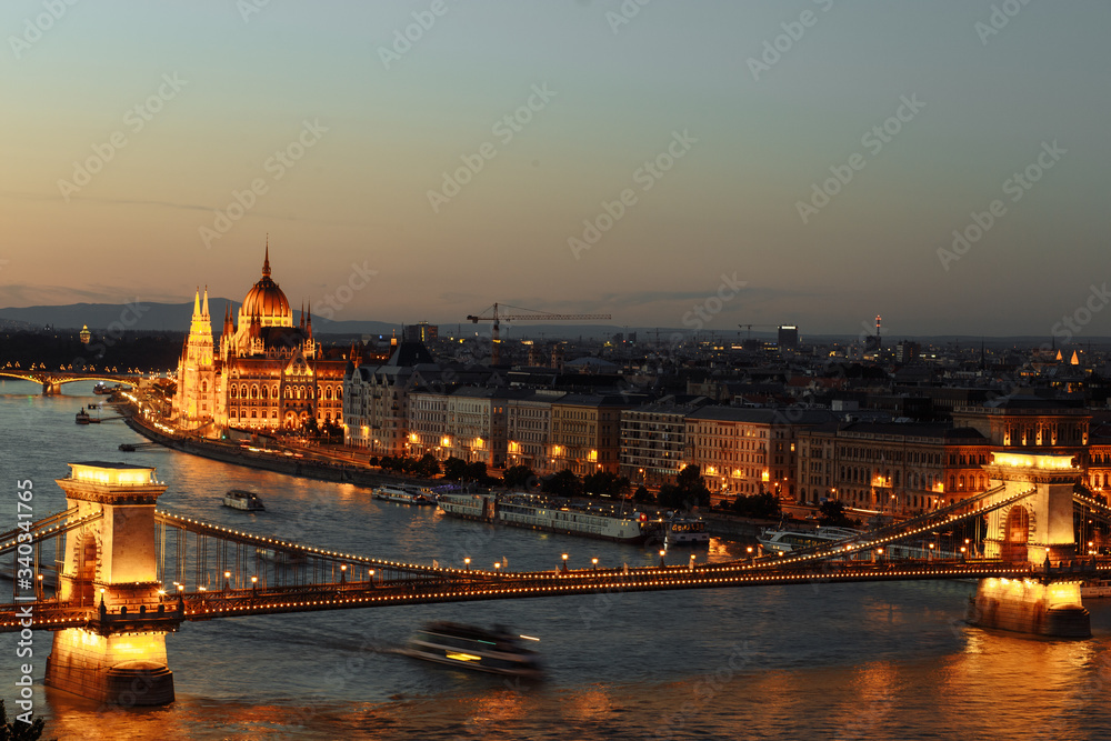 night view of the city of Budapest on the Danube river on which ships with illuminated bridge and parliament sail
