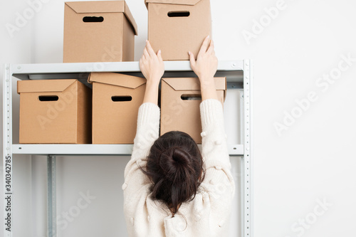 Woman put a cardboard box on a shelf of a rack in warehouse. Clean up and organize a pantry concept.