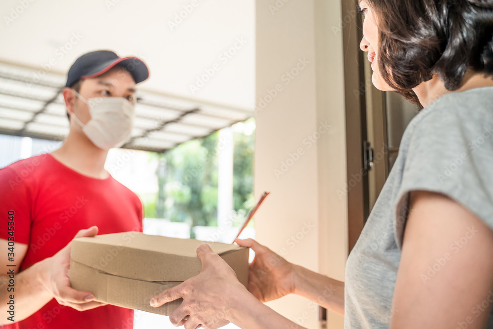 Asian postman or deliveryman carry small box deliver to young woman customer in front of door at home. Man wearing mask prevent covid or coranavirus affection outbreak. Social distancing work concept. Asian postman or deliveryman carry small box deliver to young woman customer in front of door at home. Man wearing mask prevent covid or coranavirus affection outbreak. Social distancing work concept.
