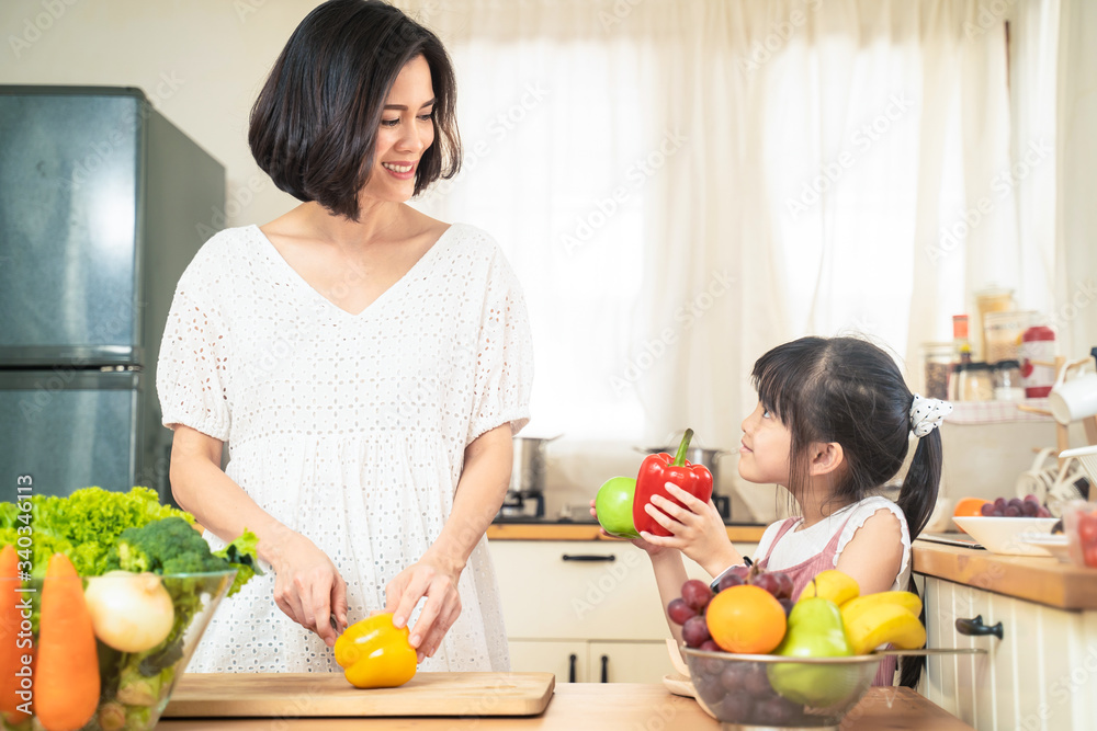 Lovely cute Asian family play, making food in kitchen at home. Portrait of smiling mother and daughter standing at cooking counter, food ingredient put on table. Happy family enjoy activity together.