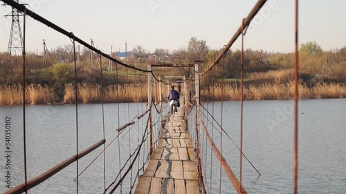 Petrovo, Dnipro / Ukraine - April 15 2020
Old suspension bridge over the river. Wooden bridge on steel cables. Village bridge. photo