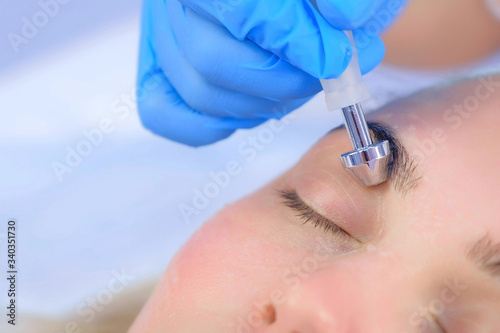 Fototapeta Naklejka Na Ścianę i Meble -  Microcurrent face treatment with hyaluronic acid gel for young woman in beauty clinic, closeup eyes. Beautician doctor moving manipula on eyelids. Apparatus hardware procedure in cosmetology.