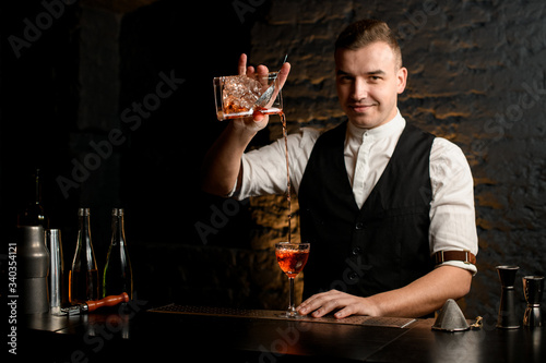 smiling young bartender at bar pours cocktail into glass