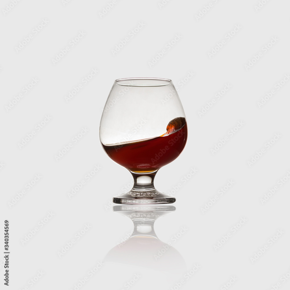 Glass with an alcoholic drink or cognac and splashes on a light background. Isolated, splash. Glass with an alcoholic drink or cognac and splashes on a light background. Isolated, splash.