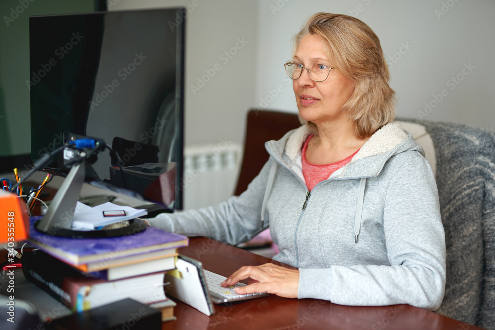 Woman middle aged in glasses using laptop typing email working at home office, lady searching information on internet or communicating online Woman middle aged in glasses using laptop typing email working at home office, lady searching information on internet or communicating online