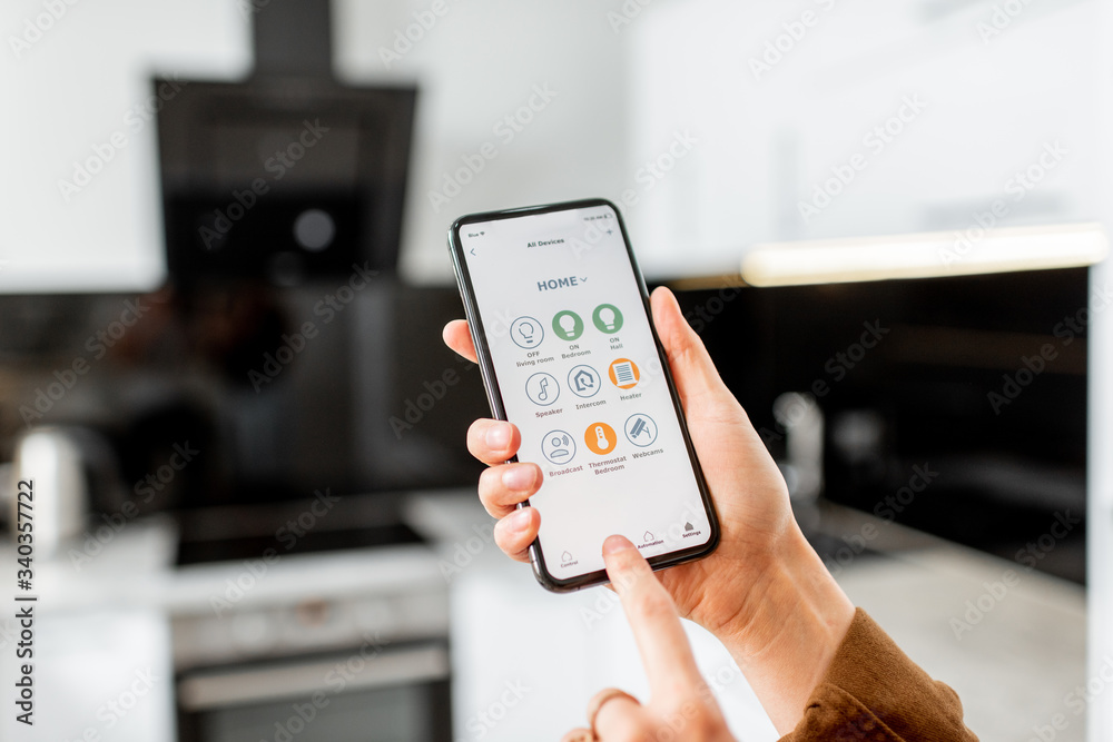 Woman controlling kitchen appliances with a smart phone, close-up on mobile device with launched smart home application. Smart home concept