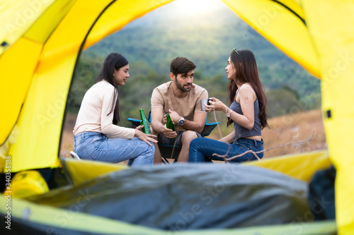 Group three Friends Camping summer concept. Group Of Friends Relaxing drinking Outside Tent and happy talk. Yellow tent is foreground.