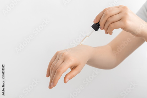 Hand of woman with pipette drop of serum or hyaluronic acid on gray background. Woman putting cosmetic serum on her hand.