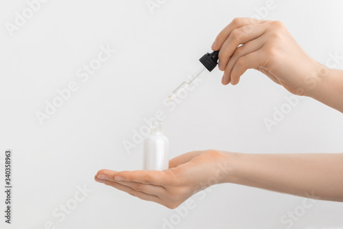 Woman hand holding pipette with collagen moisturizing hyaluronic acid serum in a white light bottle with pipette isolated on grey background.