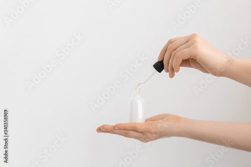 Hands of a beautiful woman dripping serum collagen moisturizer of face into clear white bottle soft light, grey background.