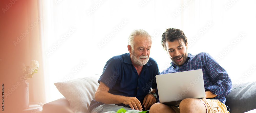 Father and son family time together at home concept. Smiling old father and happy son sitting on sofa using digital laptop computer in living room at home - obrazy, fototapety, plakaty 