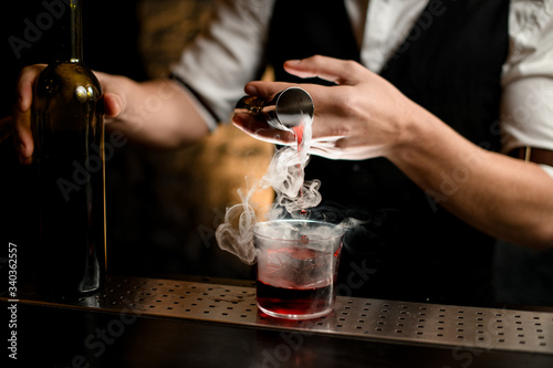 close-up. Bartender's hand pours smoky drink from jigger into glass with ice