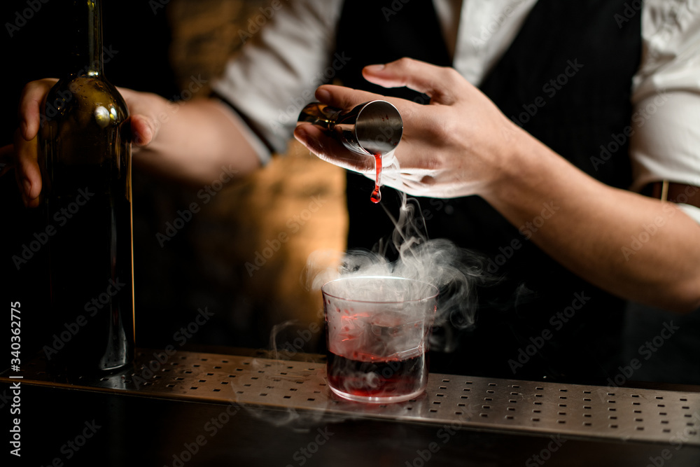 close-up. Bartender's hand gently pours smoky drink from jigger into glass with ice