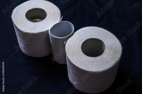 Three rolls of single-layer and thin toilet paper on a black background, two whole rolls