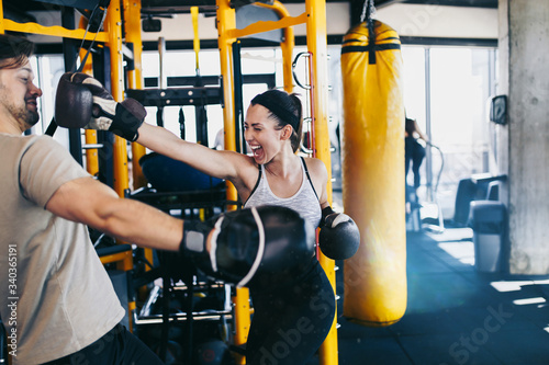 Young attractive woman with instructor on kickboxing training. She hitting or punching in big yellow boxing bag.