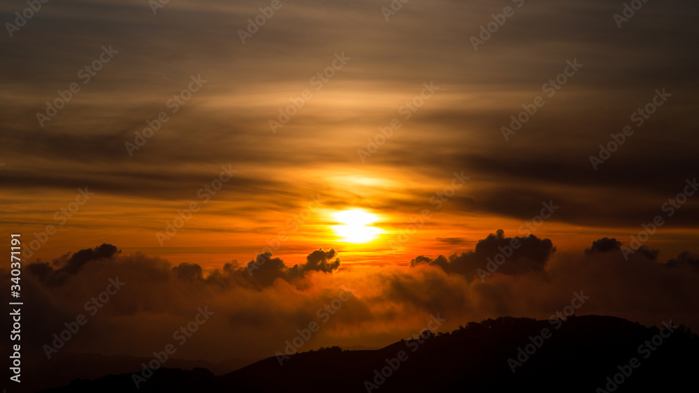 Dark Orange Sunset over Pacific Ocean in California with Dragon Cloud Shape and Hill in Foreground 