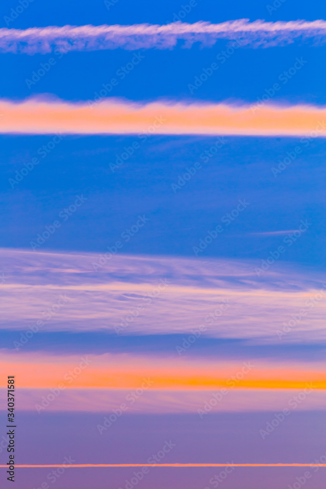 Abstract Vertical Sky at Sunset with Clouds and Plane Contrails Colored Blue, Orange, Pink and Purple