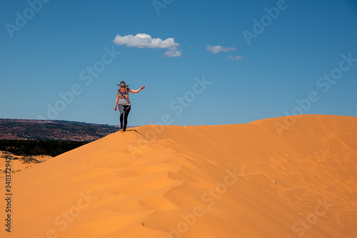 Woman walking through the Coral Sand Dunes State Park in Utah, United States. Orange, desert landscape with beautiful, blue sky. 