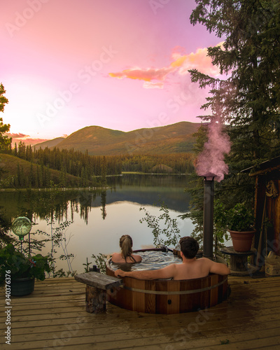 Foto Couple soaking in an outdoor hot tub overlooking beautiful, calm lake in isolated forest, woods