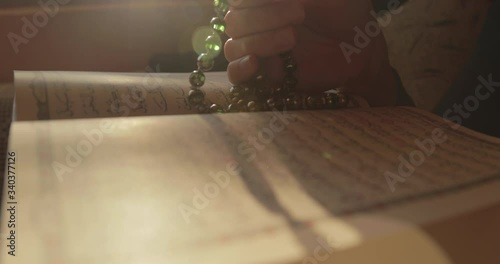 A person praying dhikr on the Muslim prayer beads with an opened Quran in the front... photo