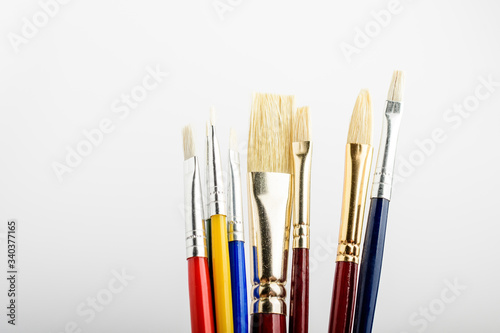 Many professional artist paintbrushes displayed vertically isolated on a white studio paper, photographed with soft focus 