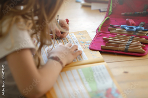 young blonde left-handed girl is training her handwriting at home on a wooden table - homeschooling concept photo