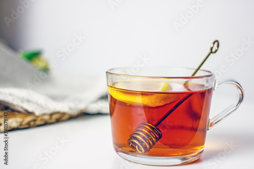 A transparent cup with black tea, a slice of lemon, a spoon for honey on a wicker gray napkin on a light table. The concept of a cozy tea party. Lemon tea in a cup. Close-up