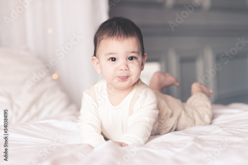 Smiling baby boy under 1 year old wearing stylish clothes lying in bed closeup. Looking at camera. Childhood.