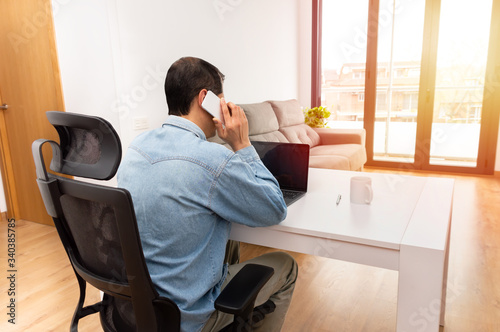 Rear view of a young businessman sitting alone in his home office and talking on his cellphone