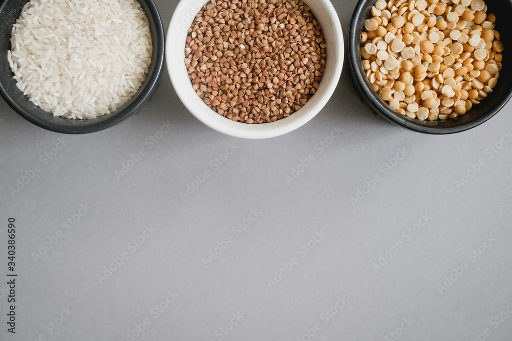 Containers of grain products, buckwheat, rice and peas in storage jars on the grey background Containers of grain products, buckwheat, rice and peas in storage jars on the grey background