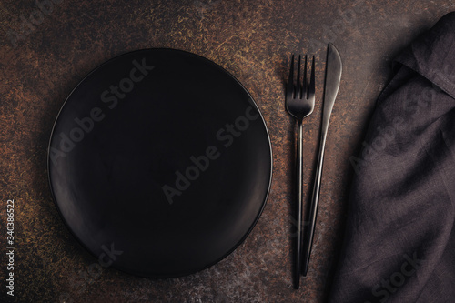 Elegant black table setting: plate, napkin and silverware over dark background. Flat lay. Top view.