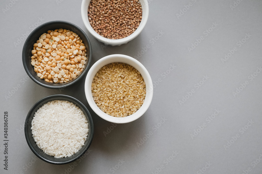 Containers of grain products, buckwheat, bulgur, rice and peas in storage jars on the grey background Containers of grain products, buckwheat, bulgur, rice and peas in storage jars on the grey background