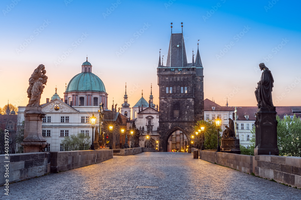 Lamps shining on the medieval stone Charles bridge with statues of saints during twilight, Prague, Czech Republic