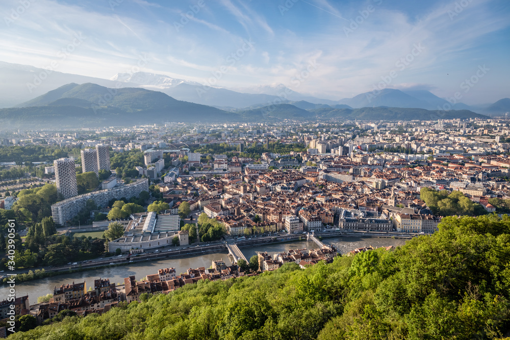 Iconic new buildings in Grenoble France on the left with the french alps in the background and the Isere river and trees in the foreground