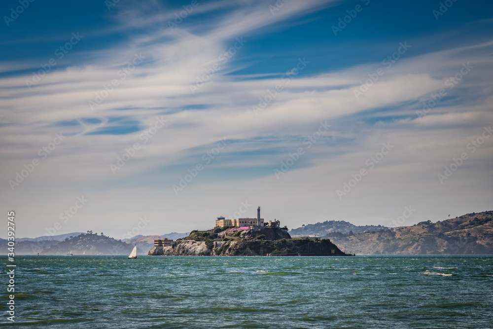 Alcatraz island with a rough misty ocean a single sailboat and dramatic clouds