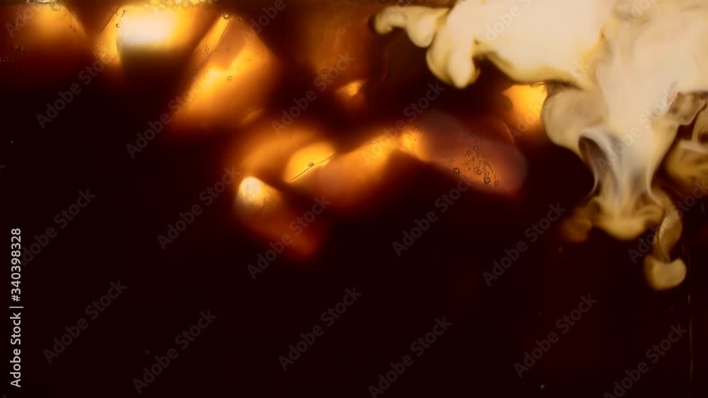 cream or milk is poured into an iced coffee, frappe, frappuccino, ice coffee. Macro. close up. slow motion. coffee ice cubes. cool drink. Making coffee. refreshing summer drink in the morning