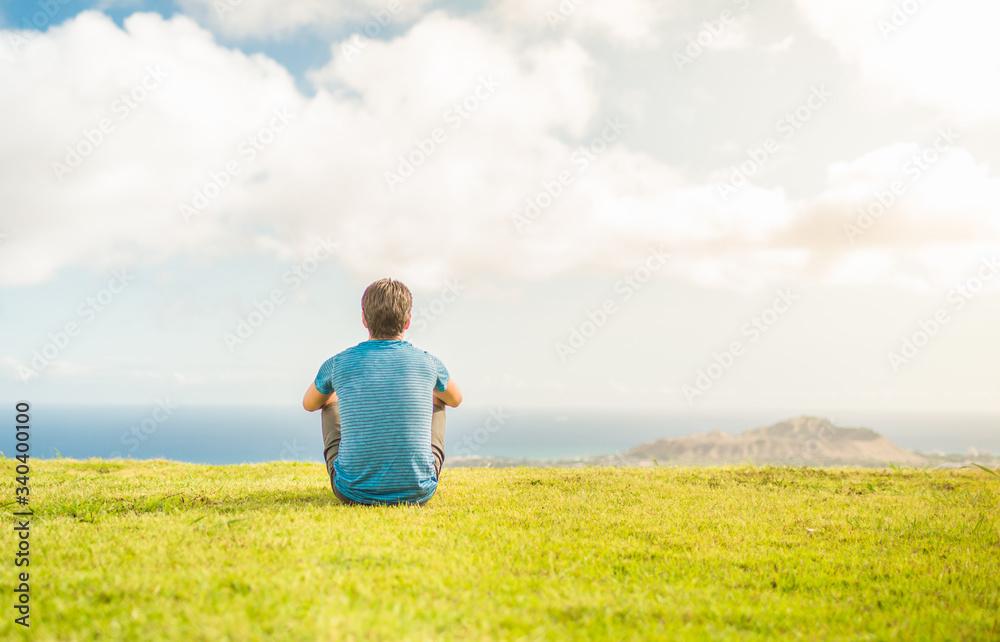 Man sitting on a field looking at the sunrise feeling at peace. 