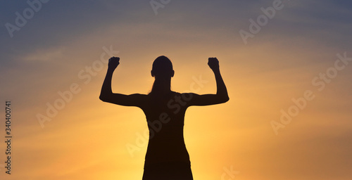 Female winning concept. Strong and confident woman silhouette flexing facing sunset sky.