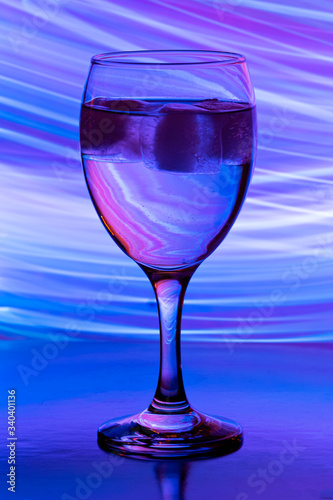 wine glass with ice on black background with neon light paintings behind
