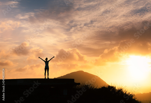 Joyful young woman standing on mountain facing the sunrise with thumbs up in the air. People feeling inspired, motivated and happy. 