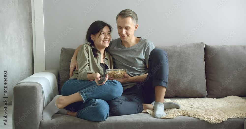Happy couple eating popcorn and watching movies on TV sitting on the couch at home. Concept of leisure and entertainment Happy couple eating popcorn and watching movies on TV sitting on the couch at home. Concept of leisure and entertainment