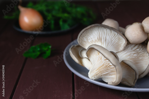 Fresh raw oyster mushrooms lie on a plate, parsley, onions on a brown wood background. Food Blog Photos.