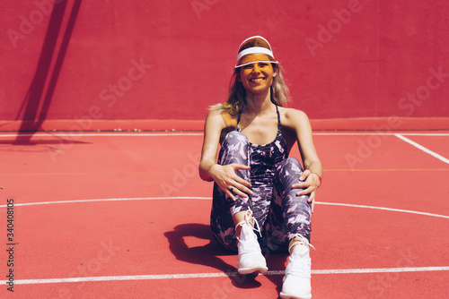 joyful sports girl in a sun visor sits on the court