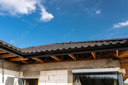 The roof of a single-family house covered with a new ceramic tile in anthracite against the blue sky, visible trusses. 