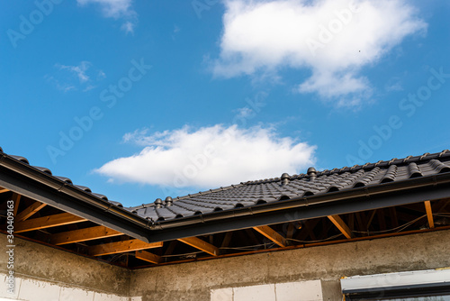 The roof of a single-family house covered with a new ceramic tile in anthracite against the blue sky, visible trusses.  © Michal