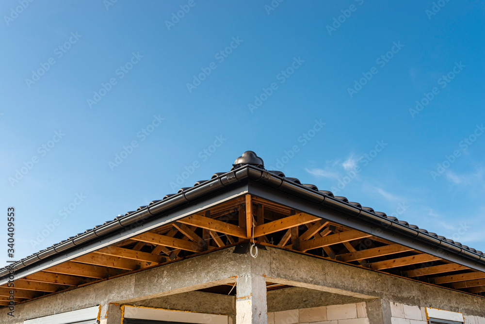 The roof of a single-family house covered with a new ceramic tile in anthracite against the blue sky, visible trusses.
